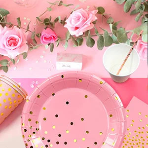 Vaisselle de fête rose et dorée à pois : assiettes près de fleurs roses.