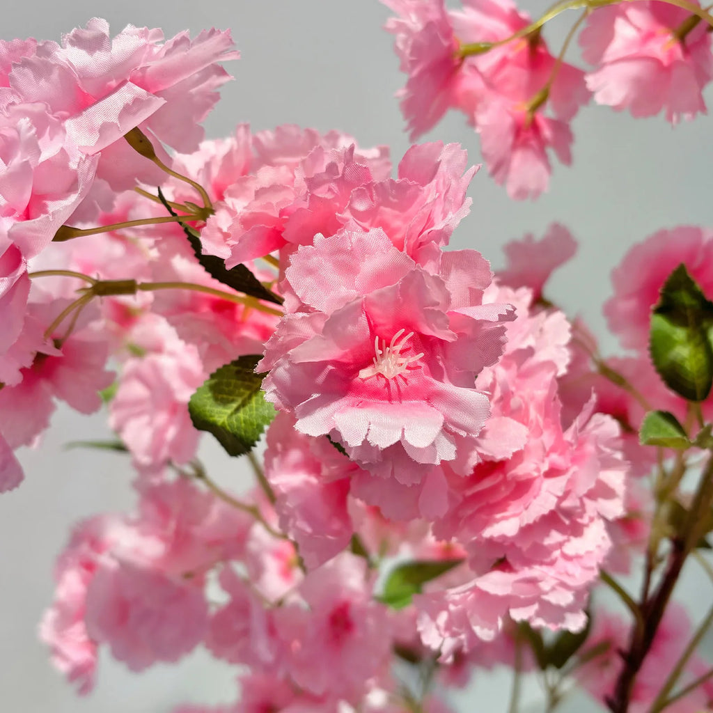 Gros plan sur fleurs artificielles de cerisier rose, pétales texturés et feuilles vertes.
