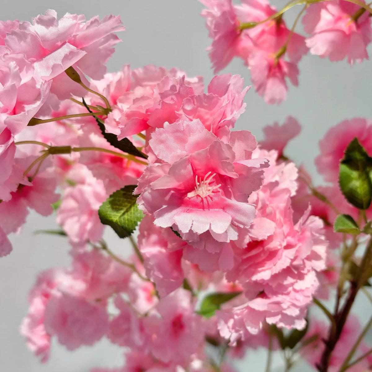 Gros plan sur fleurs artificielles de cerisier rose, pétales texturés et feuilles vertes.