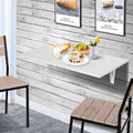 Table murale pliante blanche avec plateau, posée contre un mur, décorations visibles.