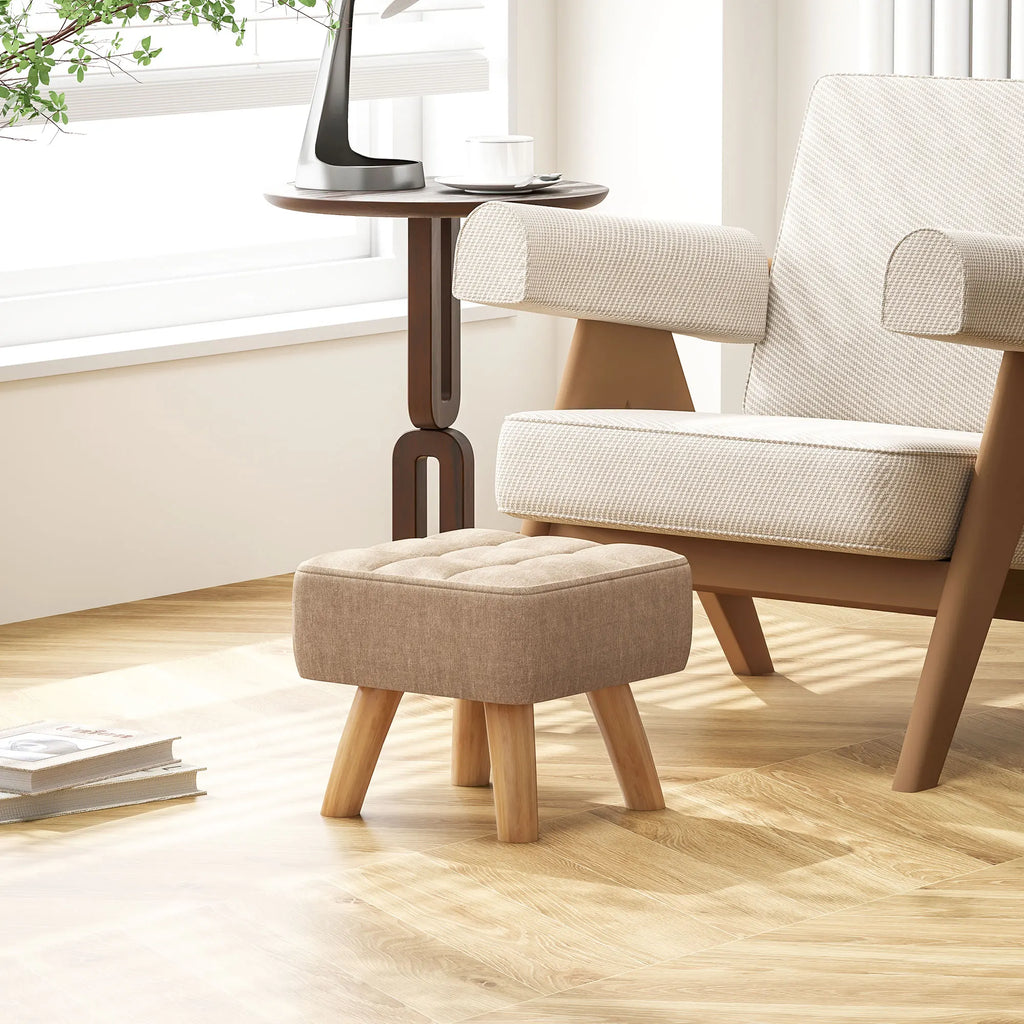 Repose-pieds beige rembourré avec pieds en bois — auprès d’un fauteuil