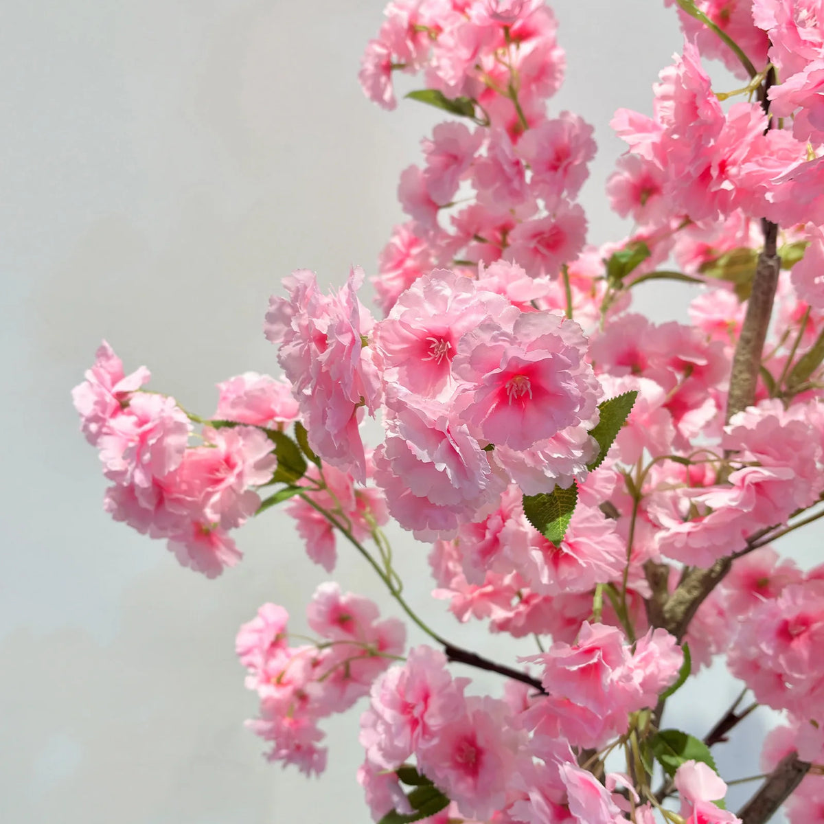 Gros plan sur fleurs de cerisier artificielles rose clair avec petites feuilles vertes.